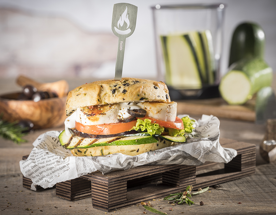 Anti – Pasti – Burger Ein köstlicher Veggie-Burger mit Zucchini, Tomaten und Salat, serviert auf einem Holzbrett auf einem rustikalen Tisch.